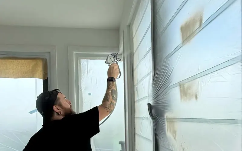 Aaron spraying interior walls with an airless sprayer, windows masked off