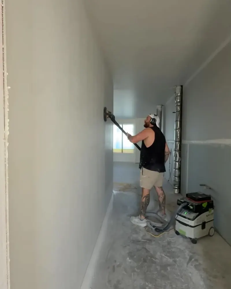 Aaron sanding walls with a long-reach sander connected to a dust extractor