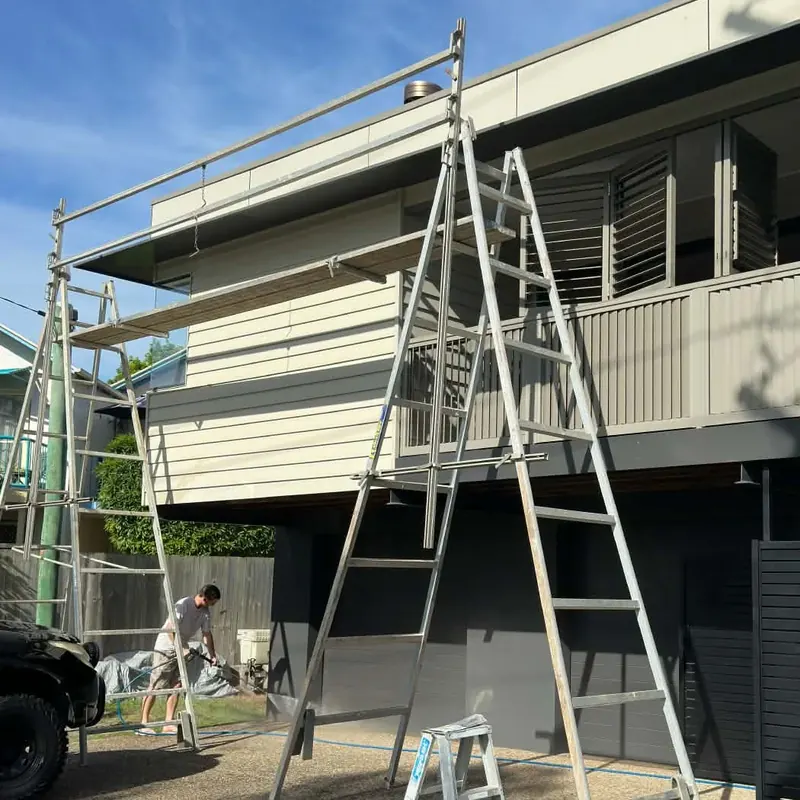 Mobile scaffold and ladders set up for exterior painting on a two-storey home