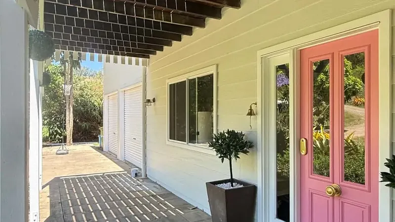 Pink front door on a covered walkway with timber beams overhead