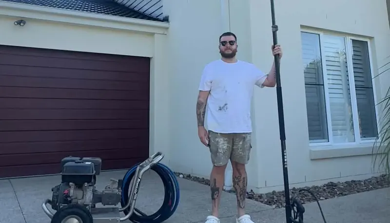 Aaron with a pressure washer and extension wand outside a two-storey home