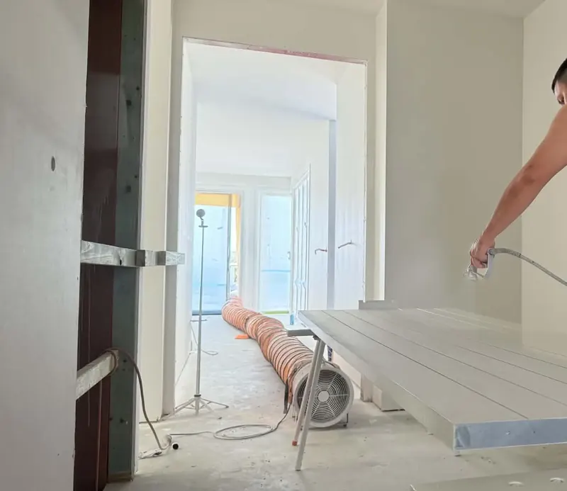 Painter spray finishing a door on trestles, with ventilation ducting set up