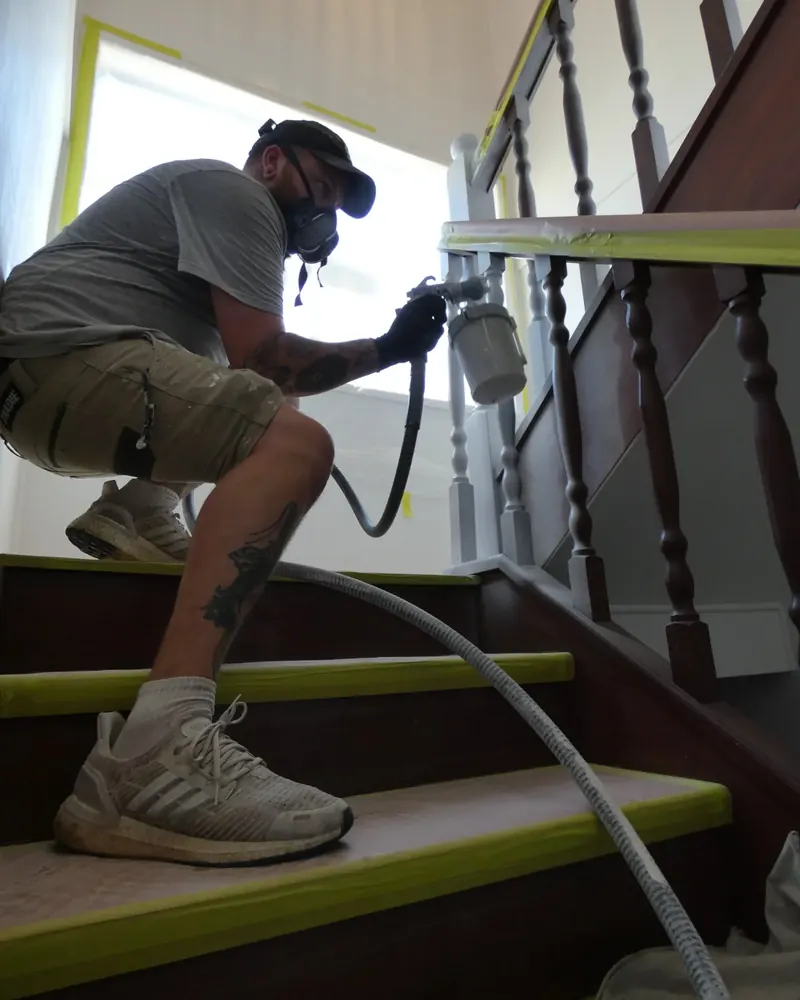 Aaron spray painting staircase balusters, with the treads masked and protected