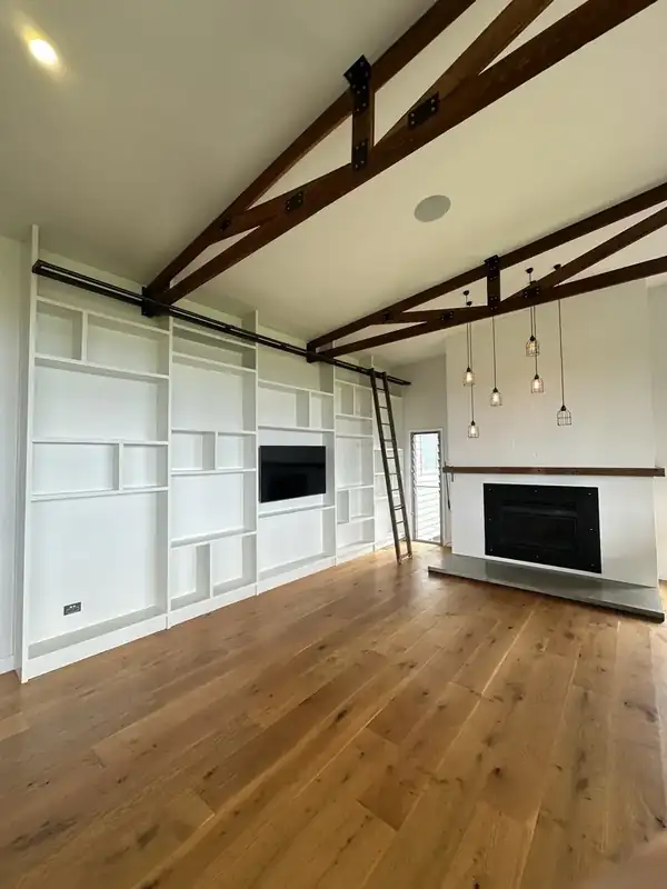 White built-in library wall with ladder, exposed timber trusses and a painted fireplace